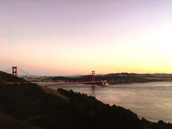 Suspension bridge over sea against sky during sunset