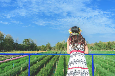 Rear view of woman standing by railing over farm against sky