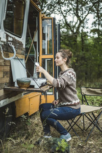 Full length of woman preparing coffee on stove by camper vehicle during camping in forest