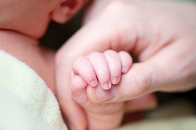 Cropped image of mother and baby holding hands at home