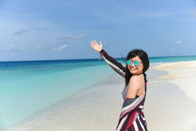 Portrait of happy woman standing on beach against sky