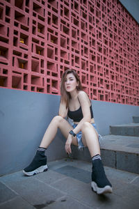 Portrait of young woman sitting against wall