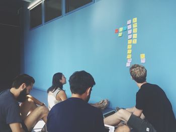 Friends looking at adhesive notes on blue wall at home