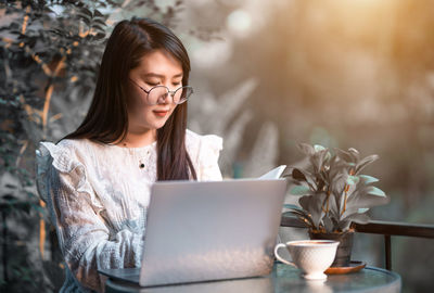 Young woman using mobile phone while sitting on table