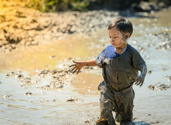 Cute boy standing in mud outdoors