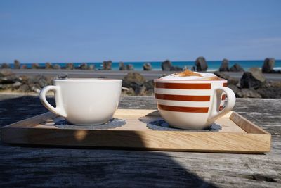 Close-up of coffee cups on wooden table against sea