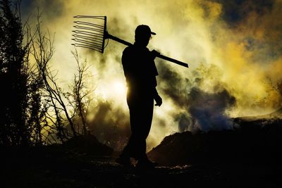 Silhouette man walking with pitchfork against sky during sunset