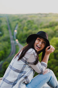 Young woman wearing hat looking up while standing outdoors