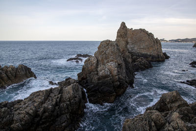 Rocks on shore by sea against sky