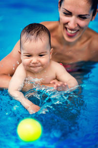 Smiling mother and son playing with ball swimming pool