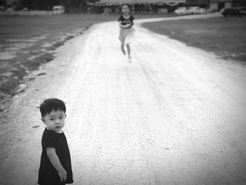 Portrait of cute toddler boy with girl running in background