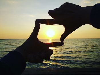 Man holding sun over sea against sky during sunset