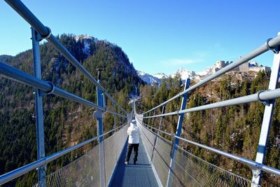 Rear view of person on suspension bridge over valley against sky