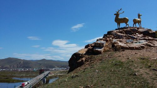 Low angle view of deer statues on hill against blue sky
