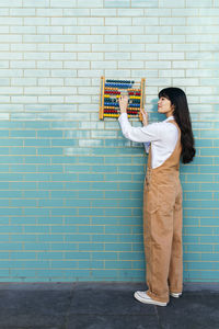 Young woman holding abacus on turquoise brick wall