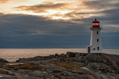 Lighthouse by sea against sky during sunset