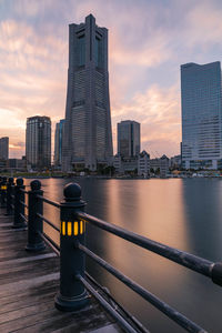 Modern buildings by the waterfront against sky during sunset.