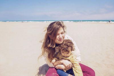 Young woman sitting on shore at beach against sky