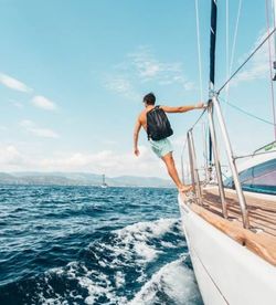 Rear view of man on sailboat sailing in sea against sky