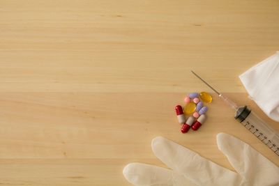 Directly above view of medicines with syringe and surgical glove on wooden table