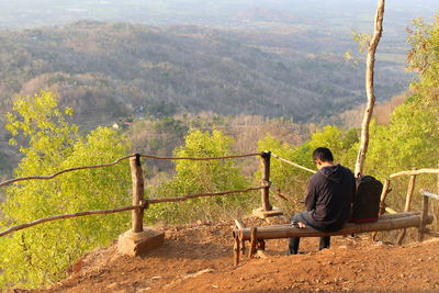 Rear view of man sitting on bench looking at mountains