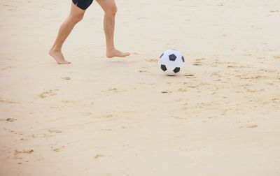 Low section of man playing with soccer ball at beach