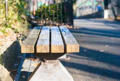 Close-up of bench on road against sunny day