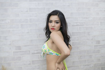 Portrait of sensuous model posing in bikini against white wall