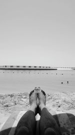 Low section of man sitting on beach against clear sky