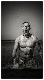 Portrait of shirtless man in sea against sky