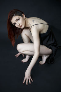 Side view portrait of beautiful young woman crouching over black background