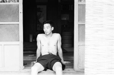 Shirtless young man sitting at doorway