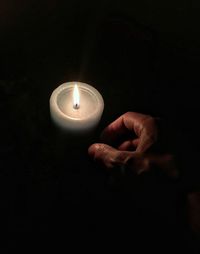 Close-up of hand holding illuminated candle in darkroom