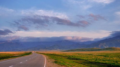 Empty road along landscape and mountains against sky