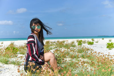 Portrait of young woman on beach against sky