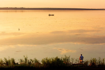 Rear view of man fishing at lake during sunset