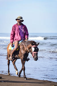 Mature man riding horse on shore at beach against sky