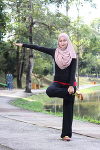 Portrait of mid adult woman wearing hijab while exercising by lake at park