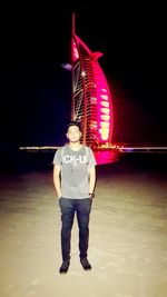 Full length of man standing by illuminated built structure against sky at night