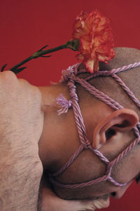 Close-up of hand holding rope tied to red flower