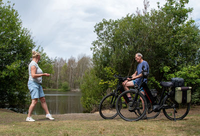 Senior couple taking a break from cycling their e bikes by a tranquil lake surrounded by lush green