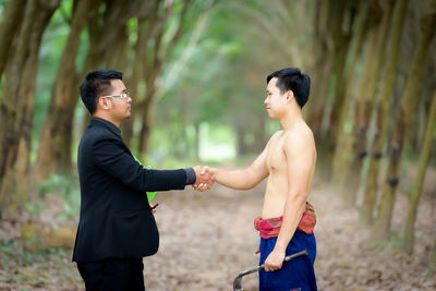 Side view of manager and shirtless worker handshaking on field