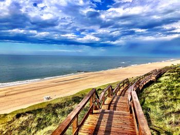 Boardwalk leading towards sea against sky