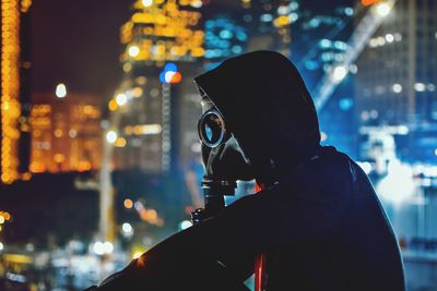 Side view of man photographing against illuminated buildings at night