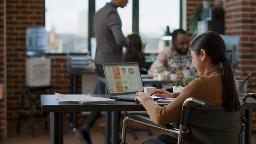 Businesswoman using laptop sitting on wheelchair