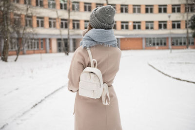 A student girl with a white backpack goes to study in winter under the snow