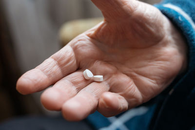 Close up view of senior male hand holding two pills while feeling bad and taking treatment