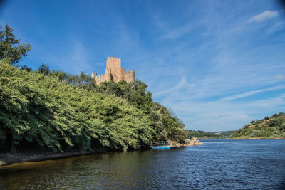 View of trees by river against sky