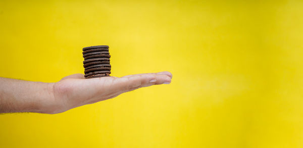 Close-up of hand holding cigarette against yellow background