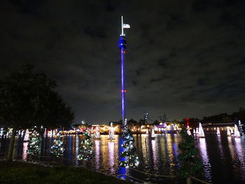 Illuminated city by river against sky at night